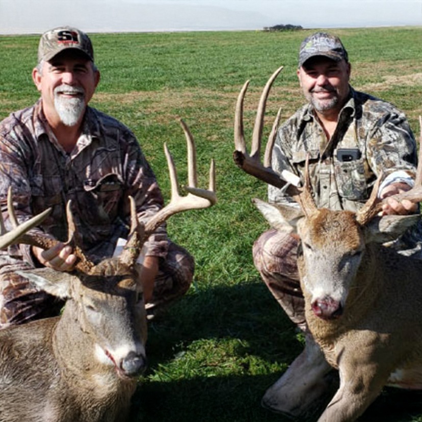 Two hunters smiling and a deer